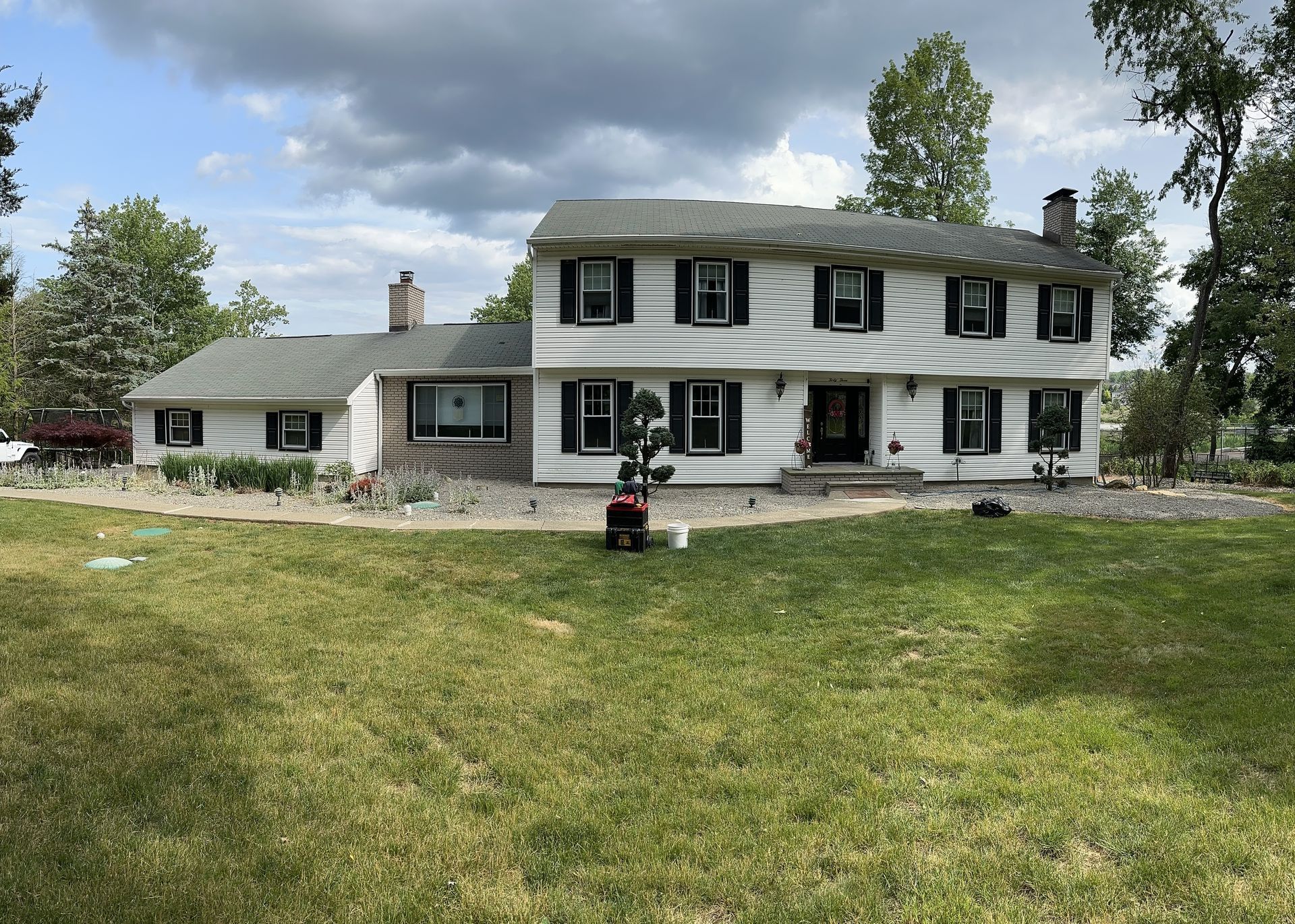 Large white two-story house with black shutters and a stone foundation on a grassy lawn under cloudy skies
