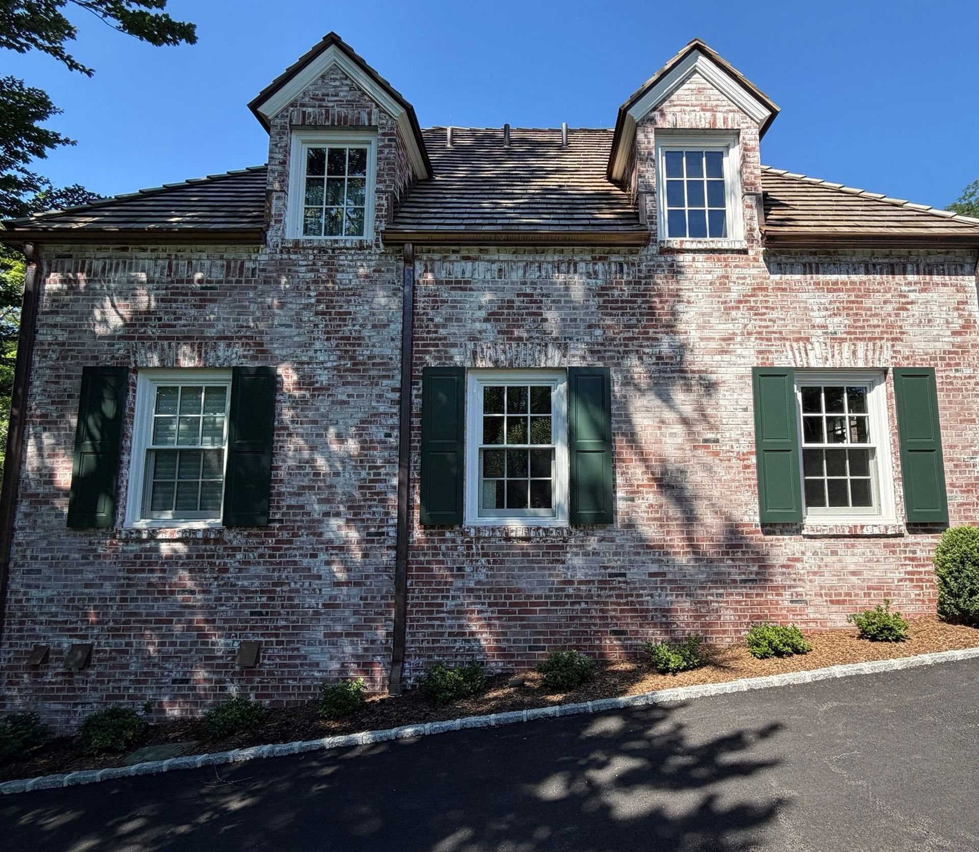 Old brick house with green shutters and dormer windows in sunlight.