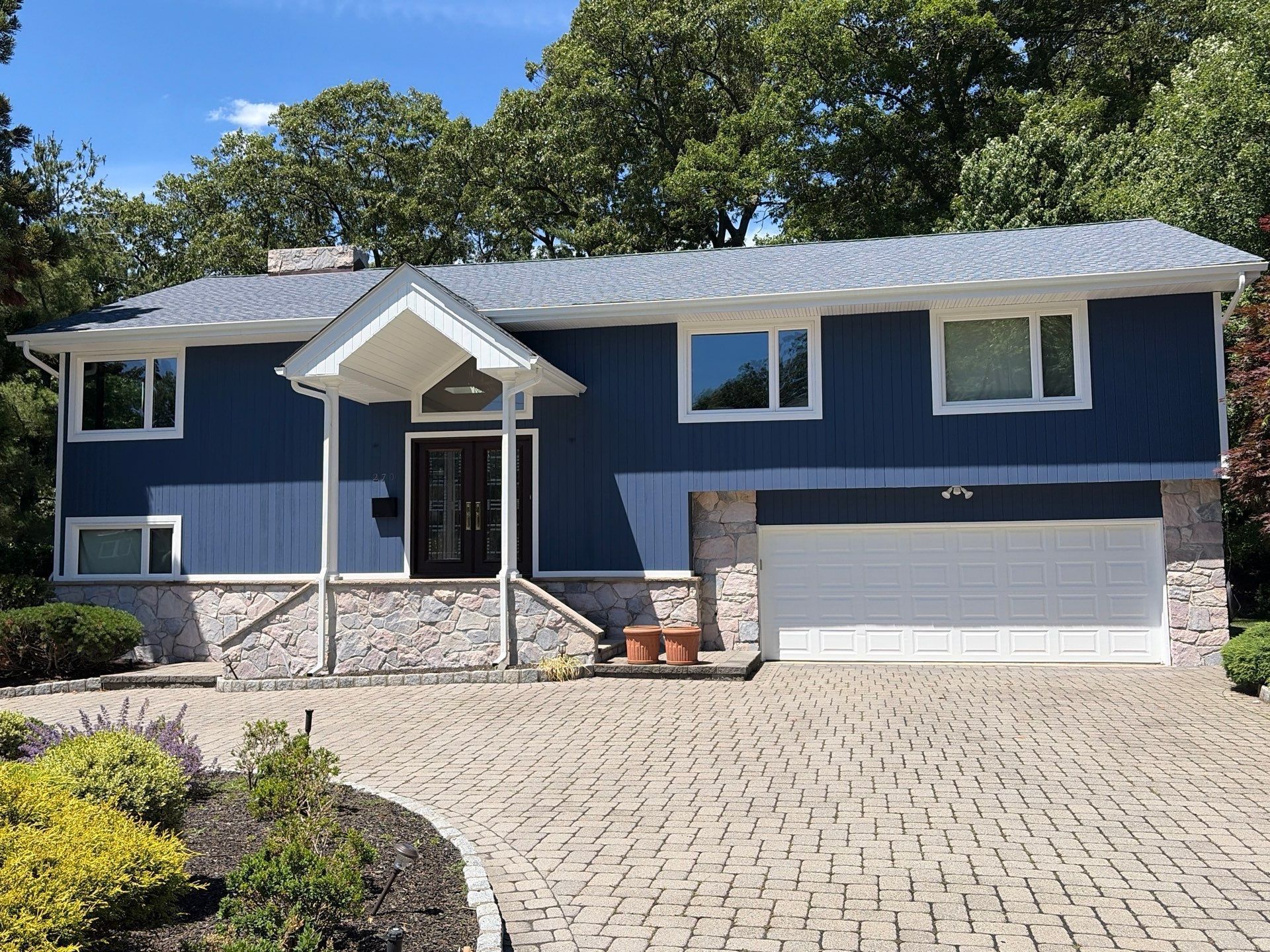 Blue suburban house with stone accents, front porch, and two-car garage under a sunny sky