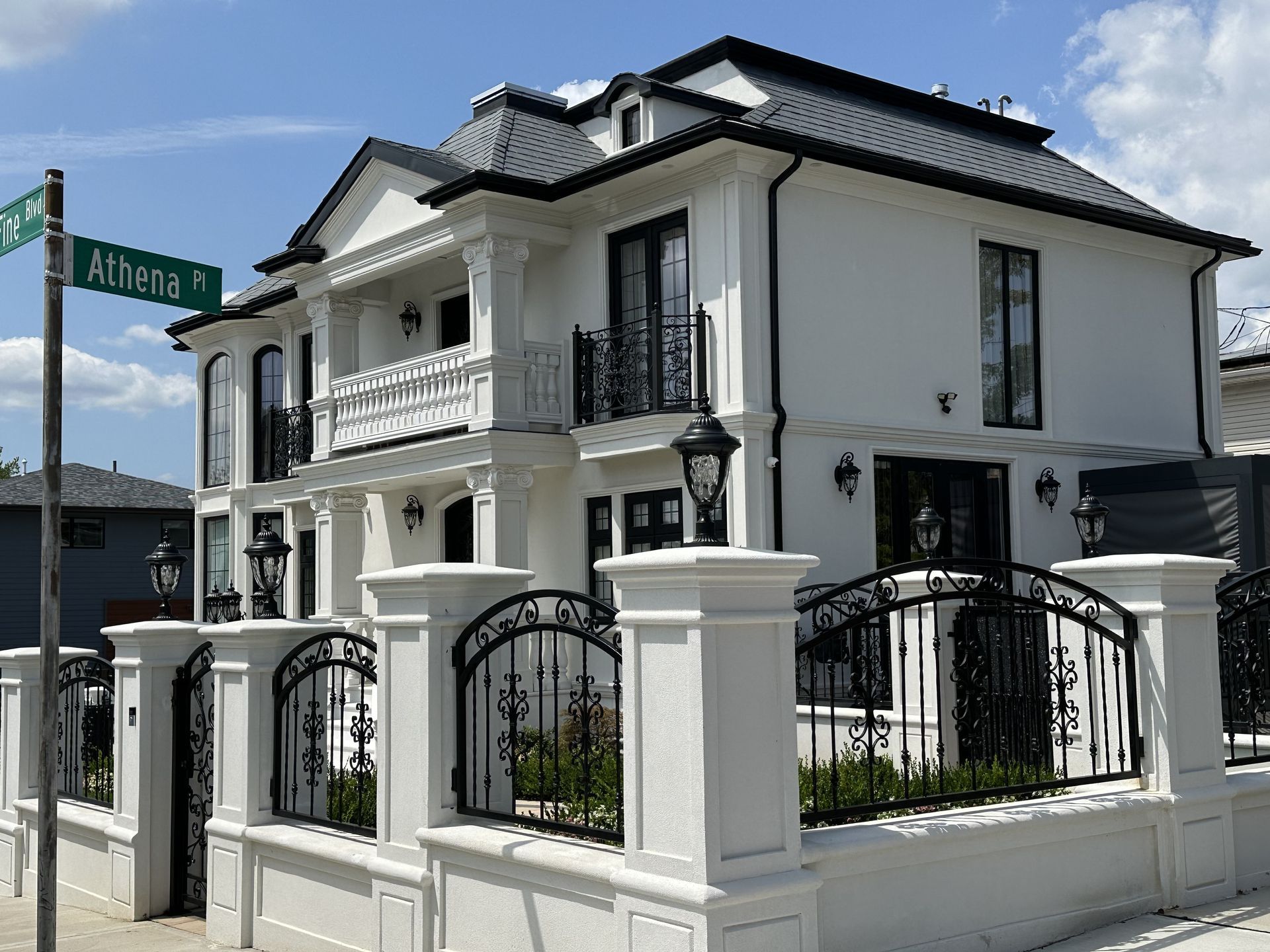 Two-story white house with black trim and wrought-iron fence on a street corner.