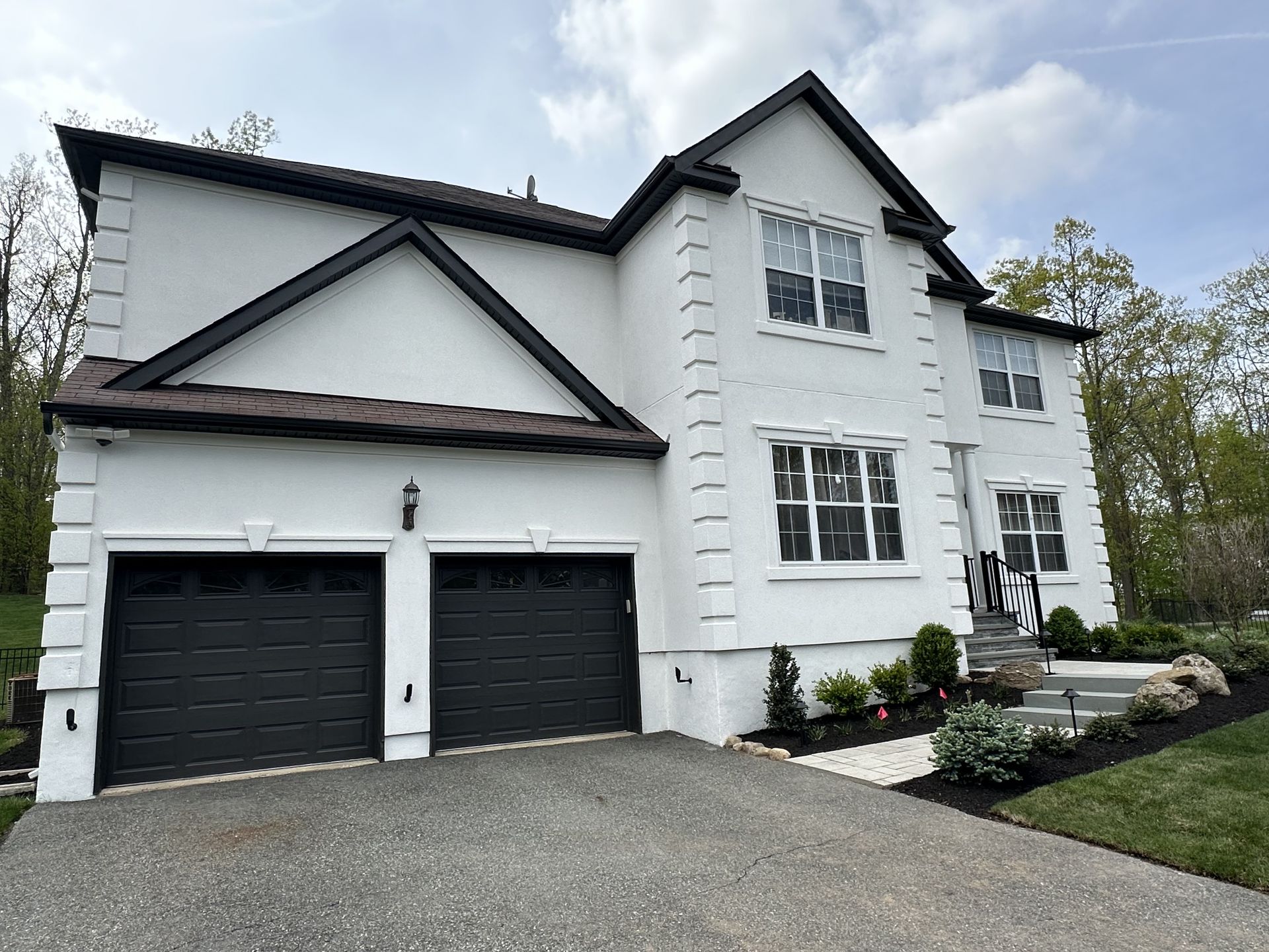 White two-story house with black garage doors, gravel driveway, and landscaped front yard.
