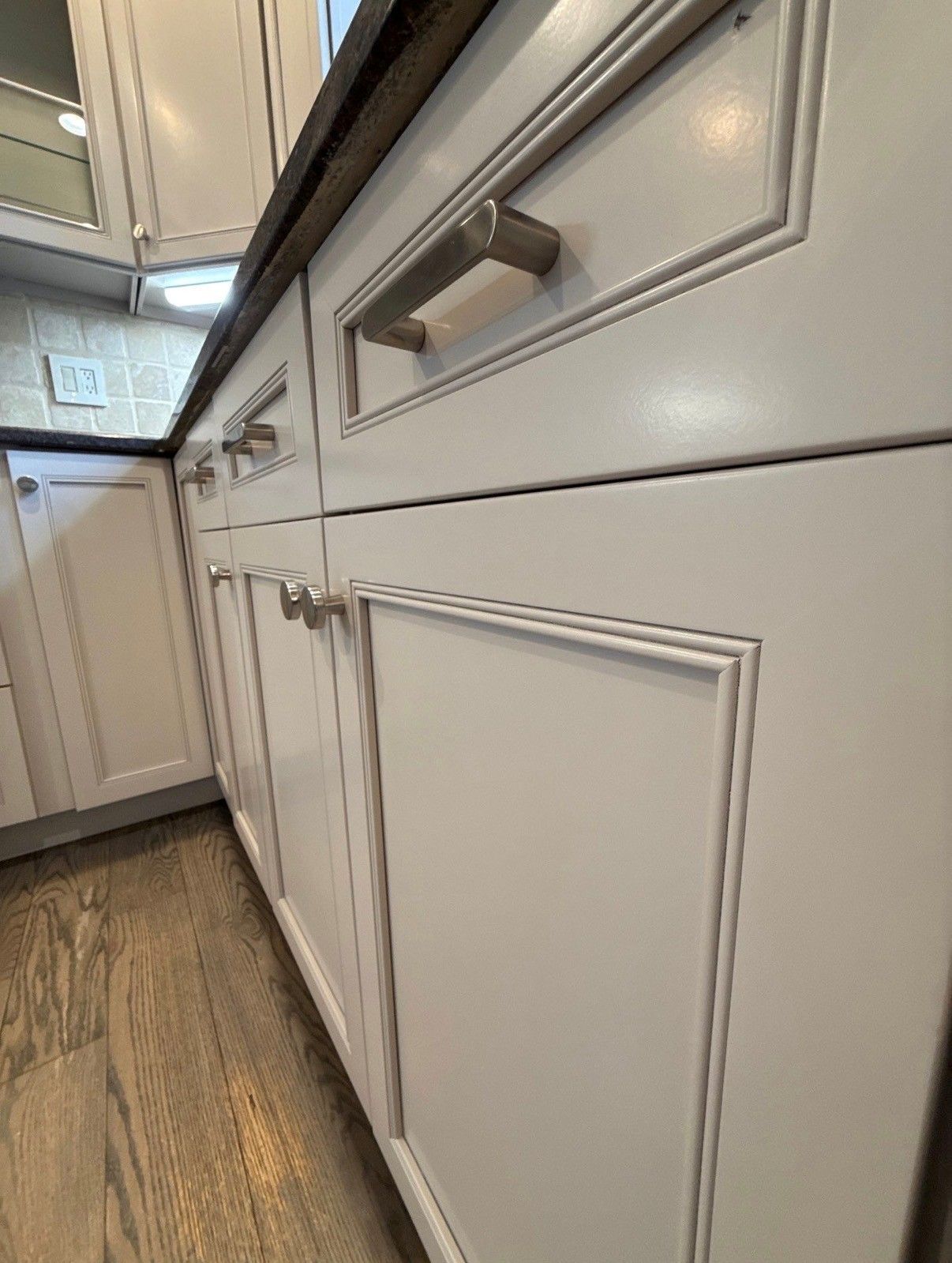 White kitchen cabinets with silver handles and wood floor in a narrow hallway view.
