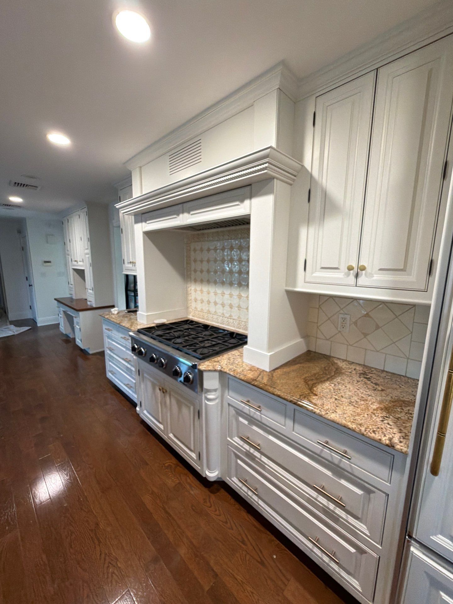 Bright kitchen with white cabinets, granite counters, stainless stove, and dark hardwood floors.