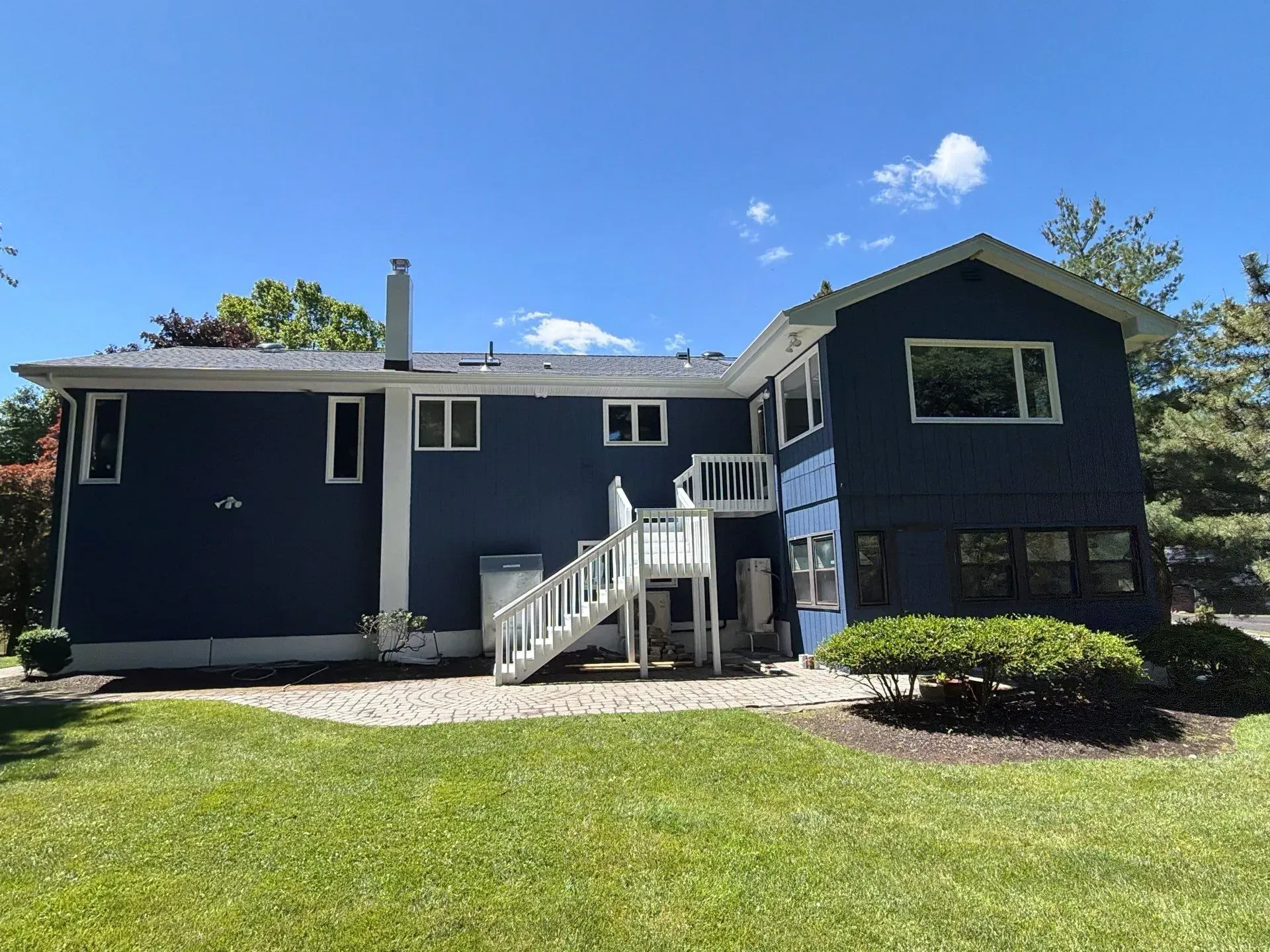 Dark blue house with white trim, front steps, and a green lawn under a bright sky.