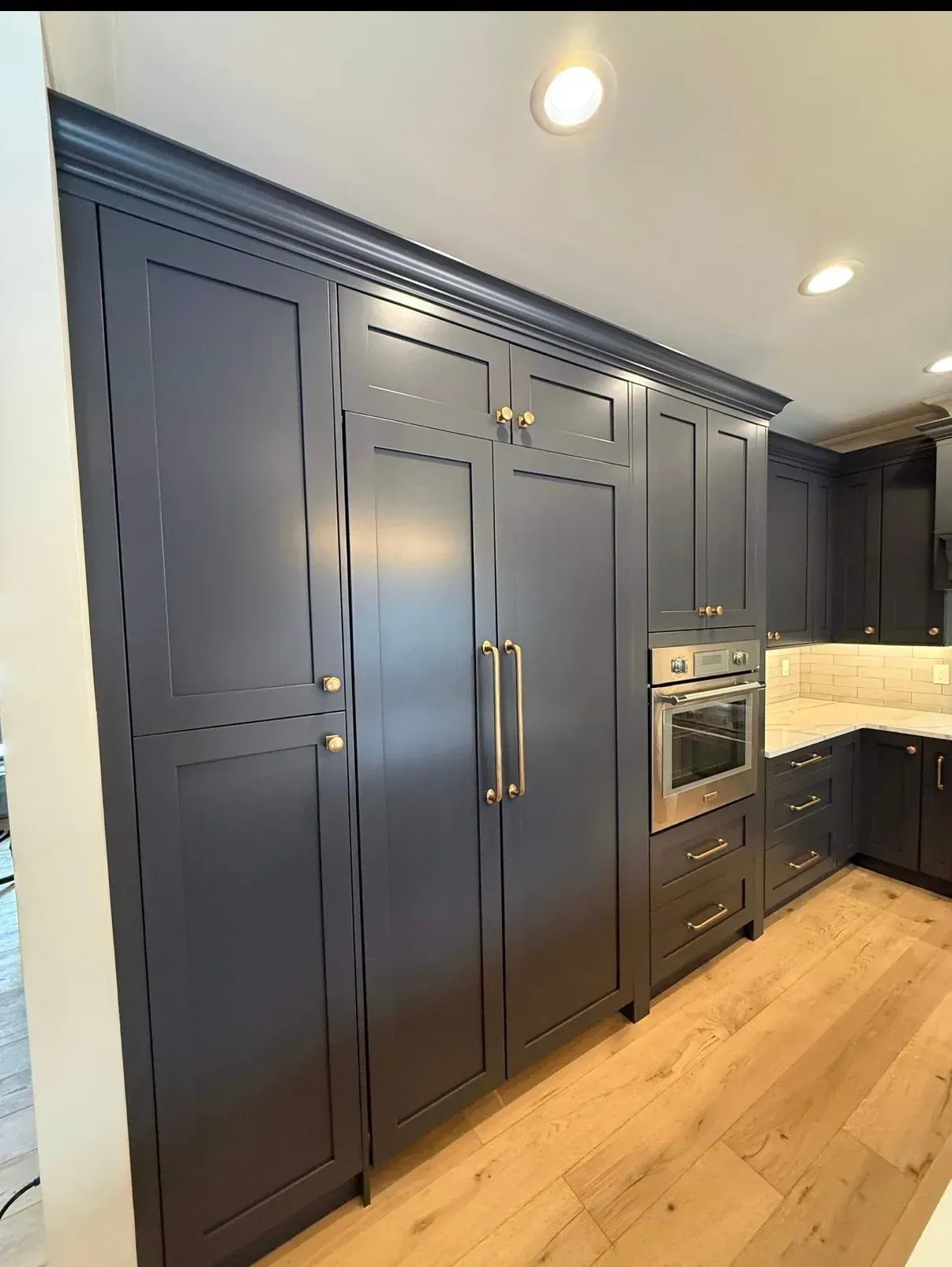 Modern kitchen with dark navy built-in cabinets, stainless appliances, and light wood floors.
