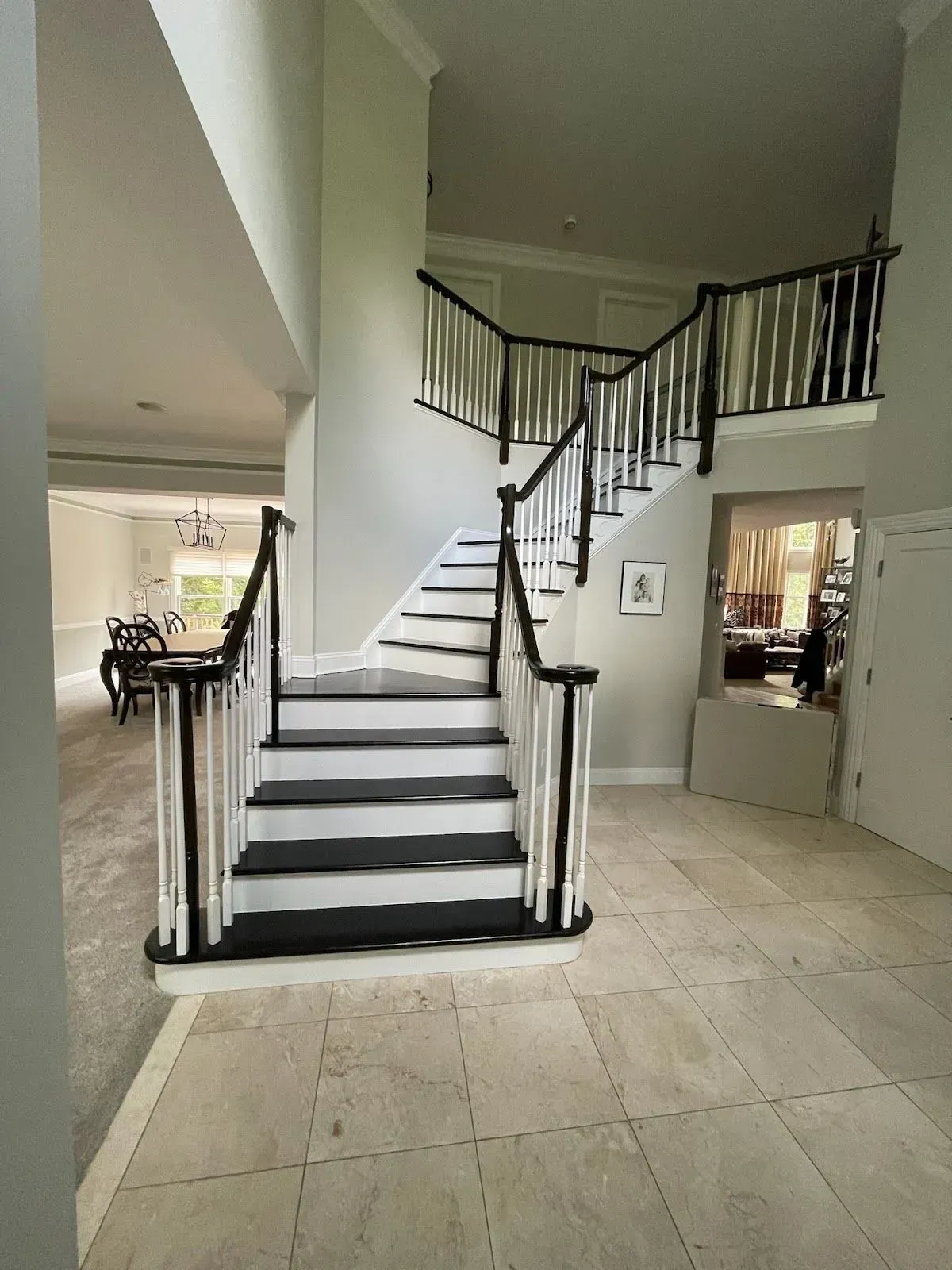 Grand foyer with curved staircase, black railings, and cream tile flooring.