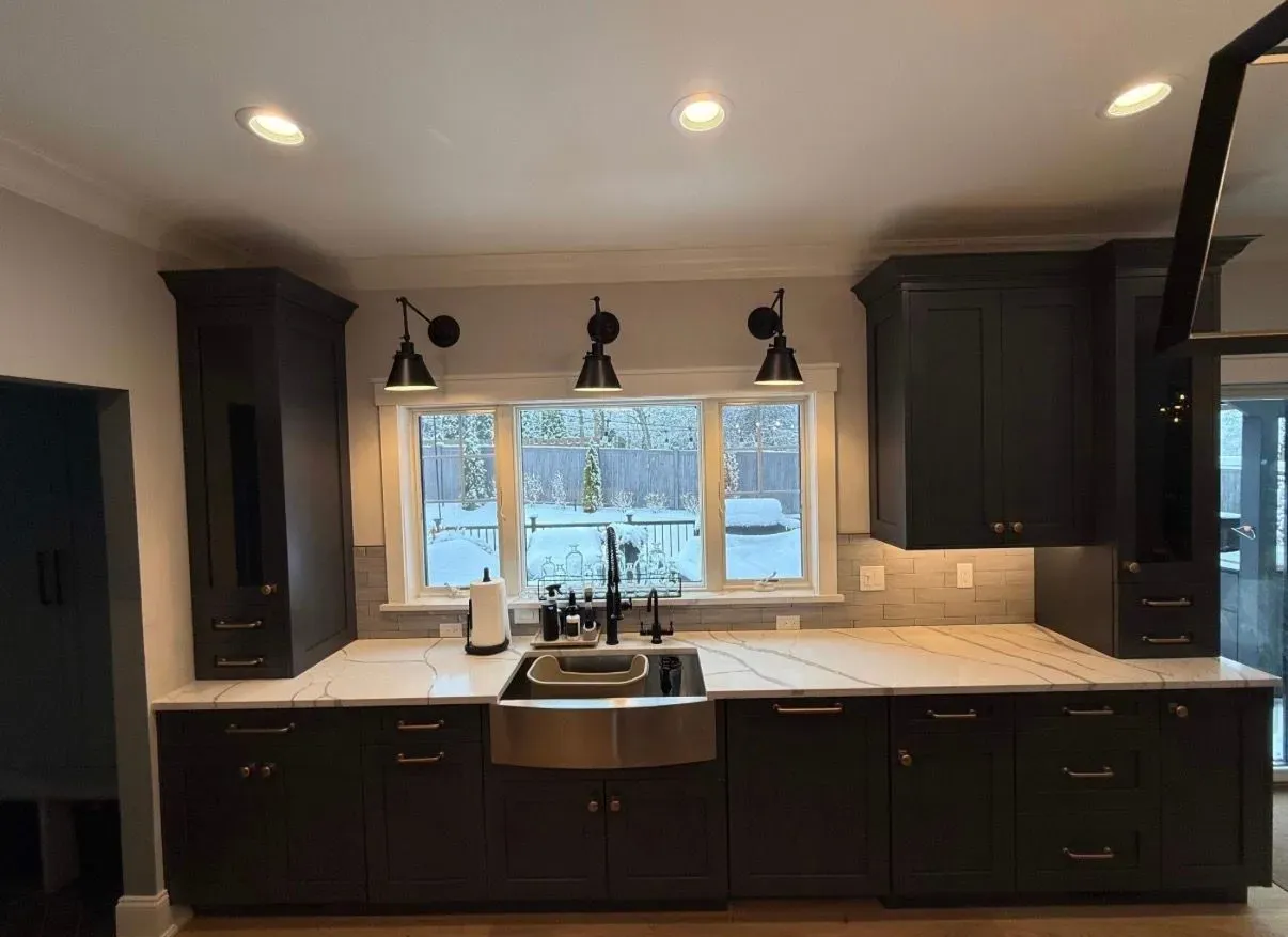 Modern kitchen with dark cabinets, white countertops, sink under a window, and pendant lights above the island.
