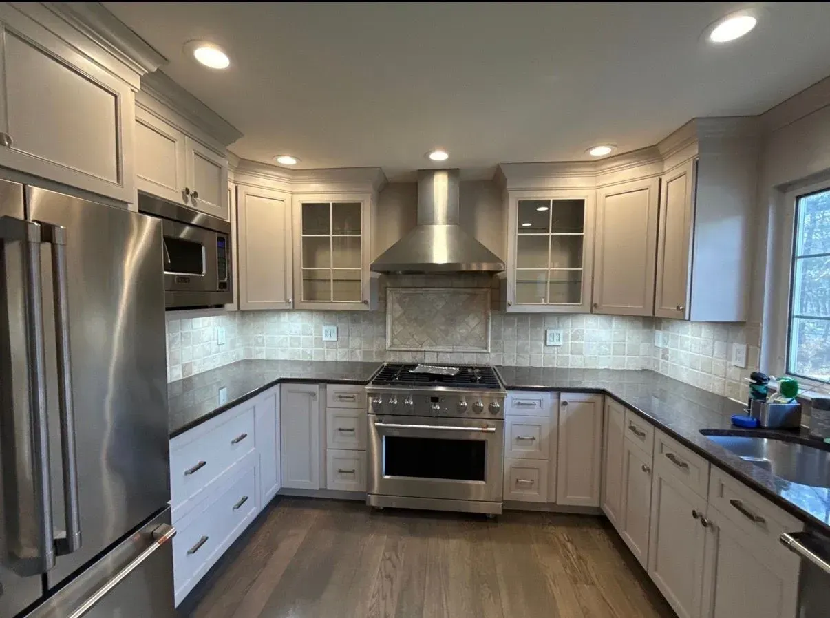 Modern kitchen with stainless steel appliances, white cabinets, and wood flooring.