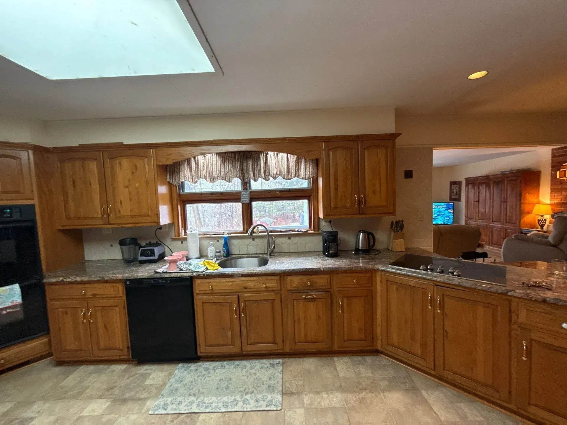 Spacious kitchen with wooden cabinets, granite counters, sink under window, and black appliances.