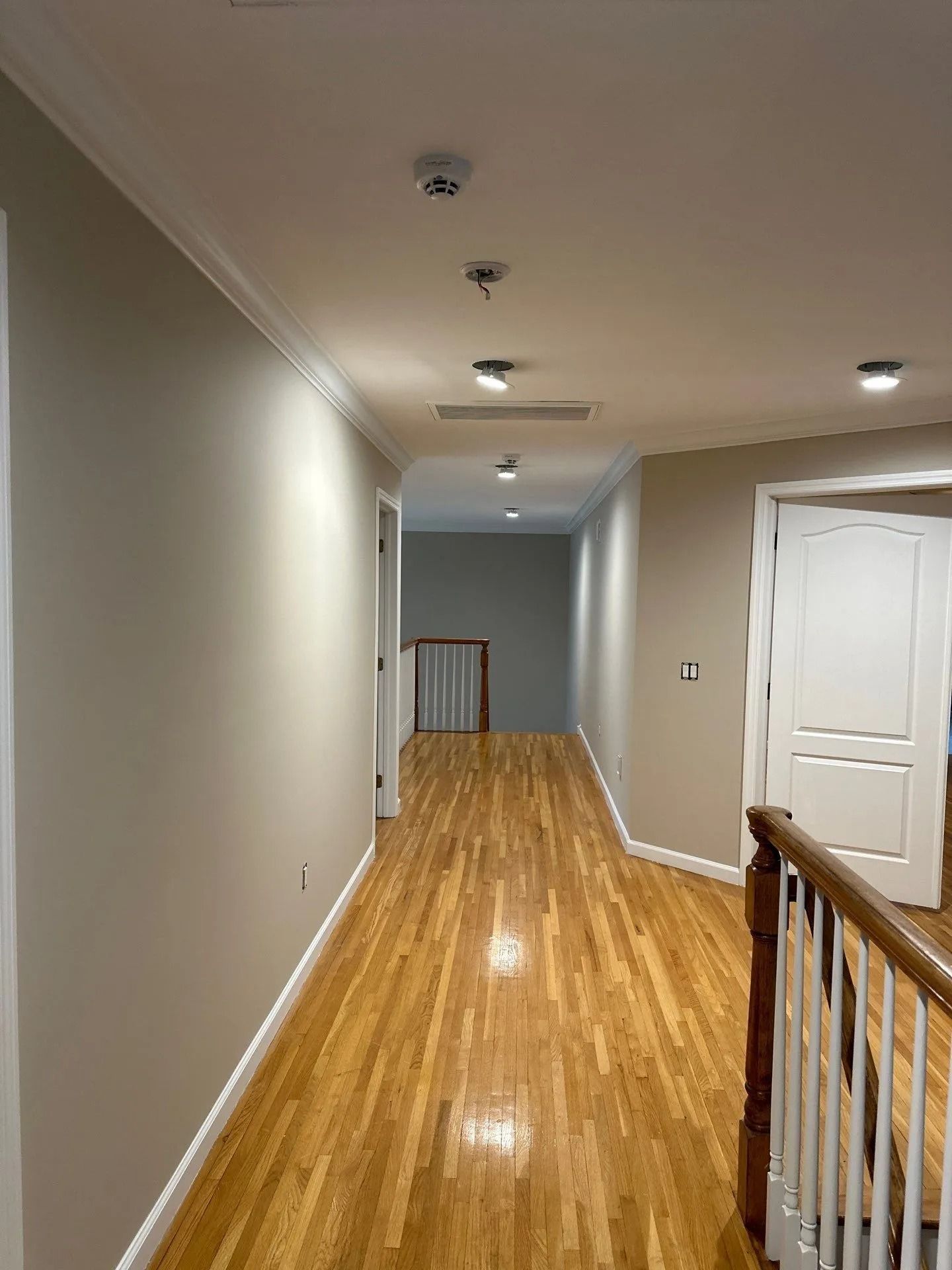 Long hallway with beige walls, wood floors, ceiling lights, and white doors in a home interior