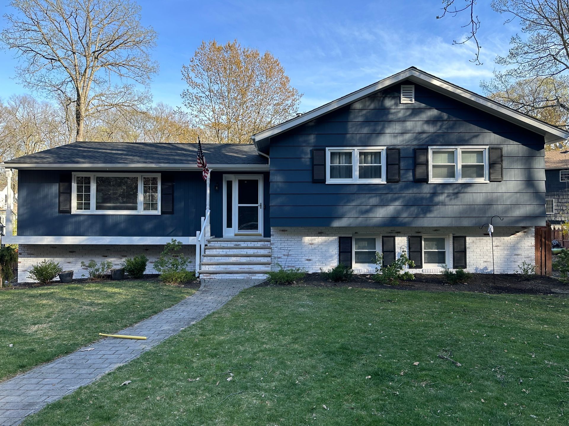 Gray house with blue trim, front steps, and a walkway across a green lawn under trees