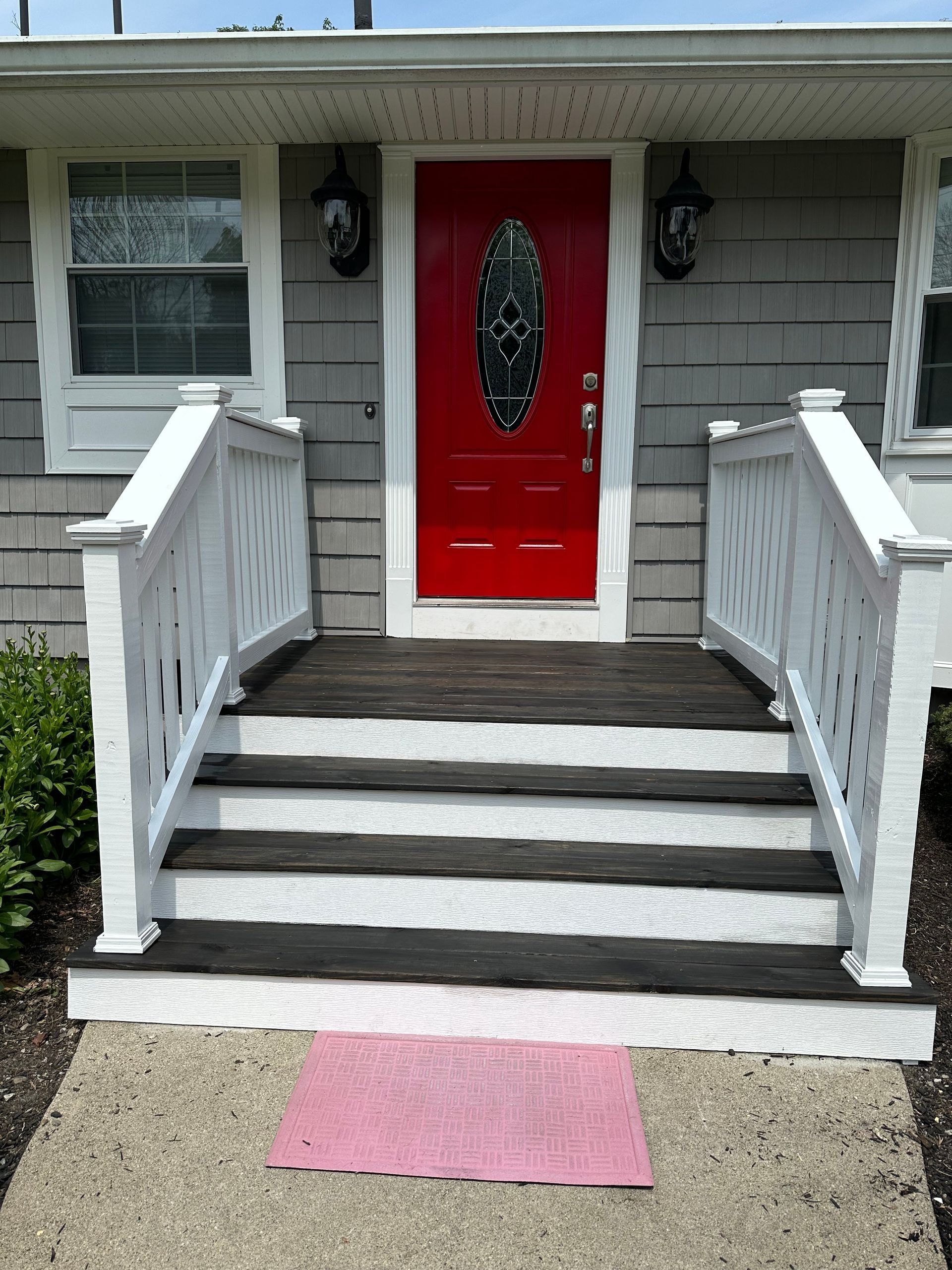 Front steps to a house with white railings, a bright red door, and a pink mat on the walkway.