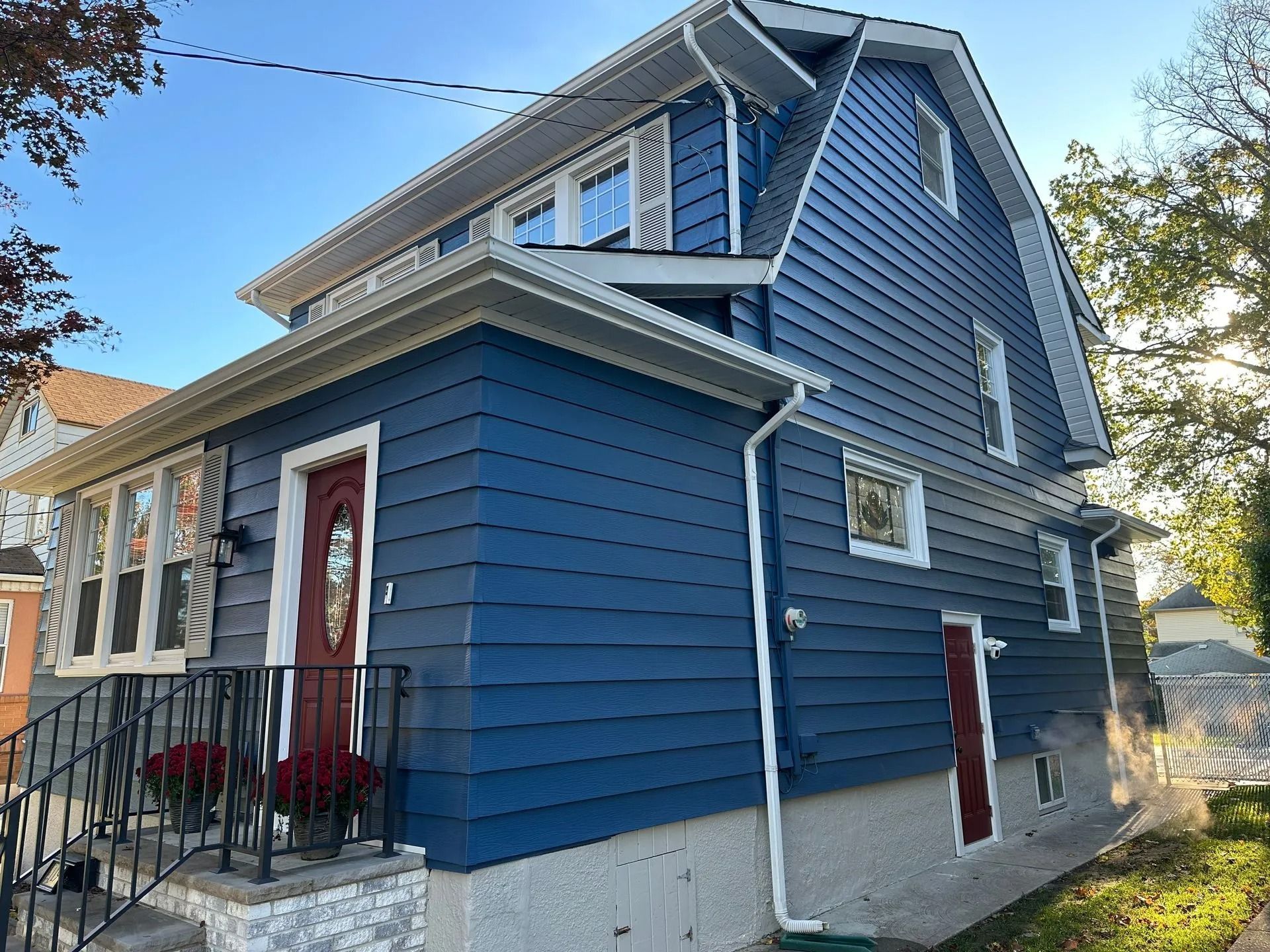 Blue house with white trim and red doors, viewed from the side on a sunny day.