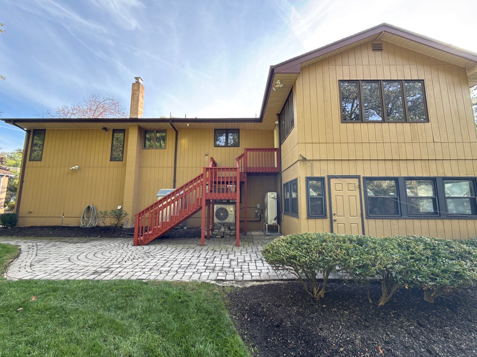 Yellow two-story house with red staircase and cobblestone walkway under a blue sky