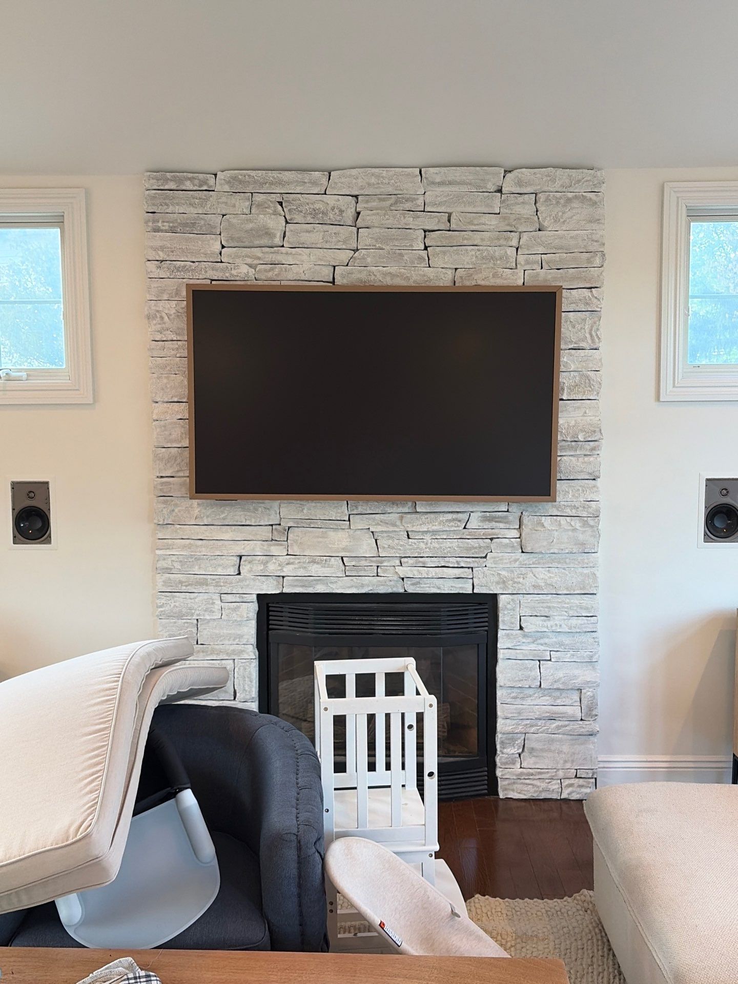 Empty living room with stone fireplace, hardwood floors, ceiling fan, and large windows with blinds