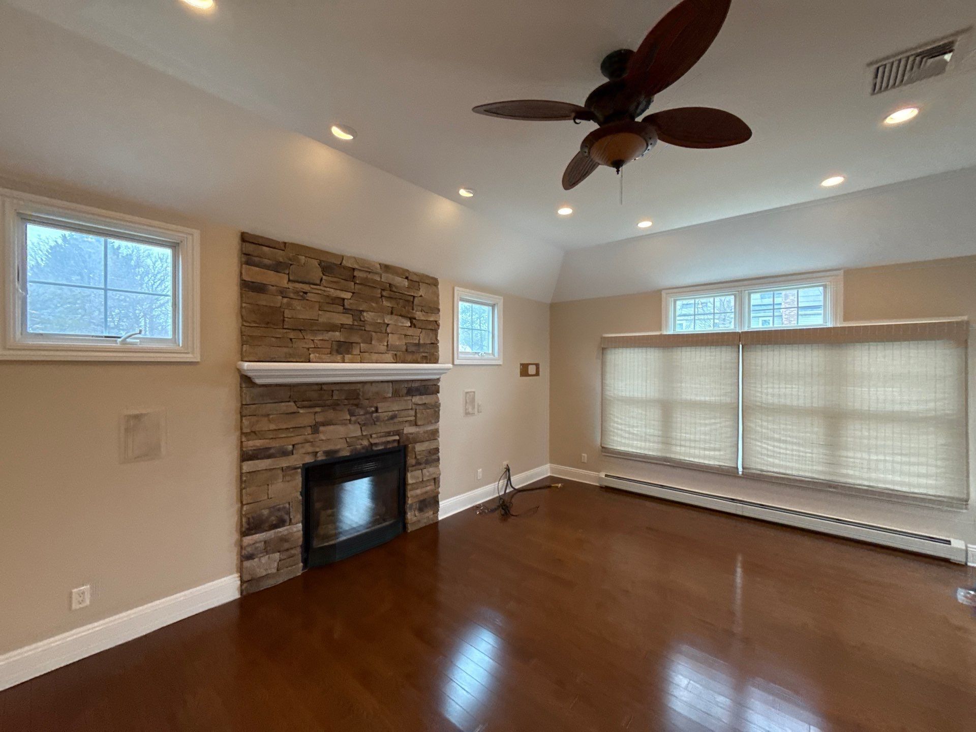 Living room with a mounted TV above a white stone fireplace, flanked by small windows and armchairs.