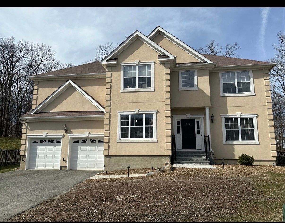 Two-story beige suburban house with a double garage and front walkway under a clear sky