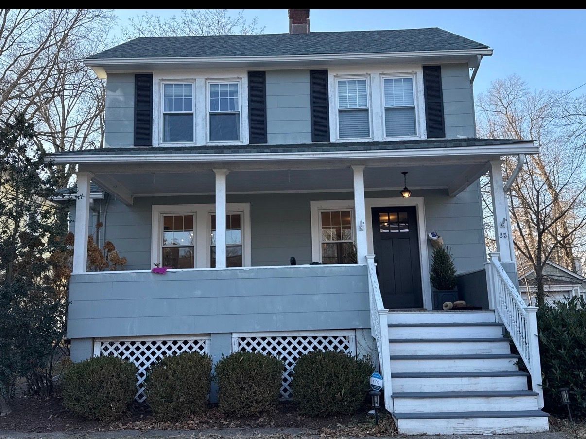 Gray two-story house with white porch and front steps, seen from the street.