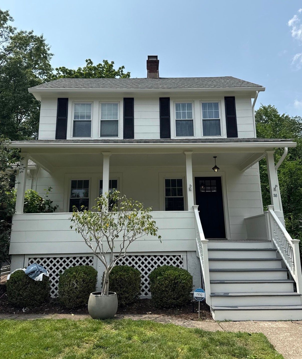 White two-story house with black shutters, front porch, and right-side stairs under a sunny sky