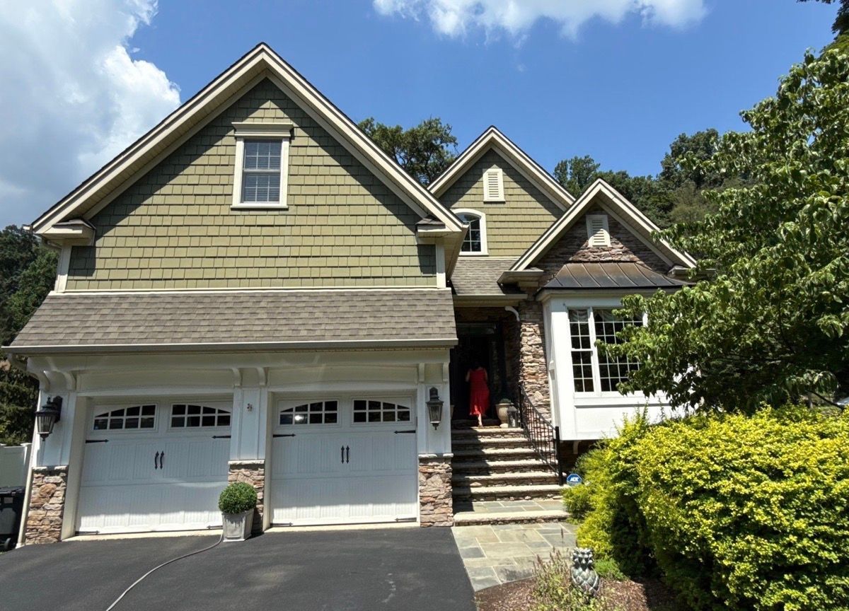 Suburban house with beige siding, two-car garage, stone steps, and a front porch under a blue sky