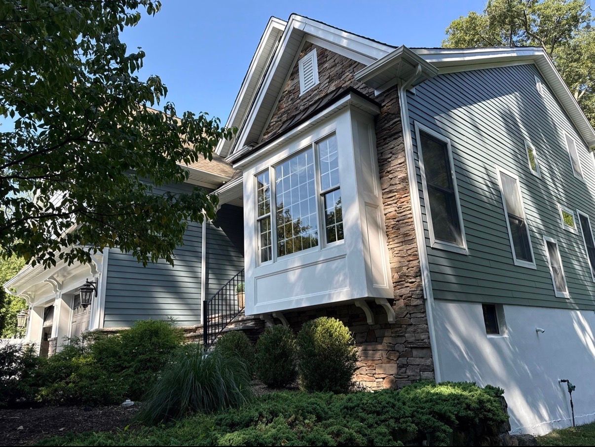 Suburban house with a stone bay window, green siding, and trees in front