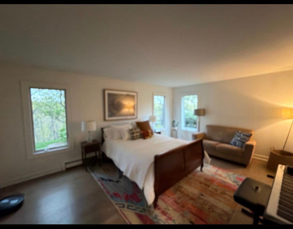 Bright bedroom with a large bed, gray walls, windows, dresser, and a ceiling light.