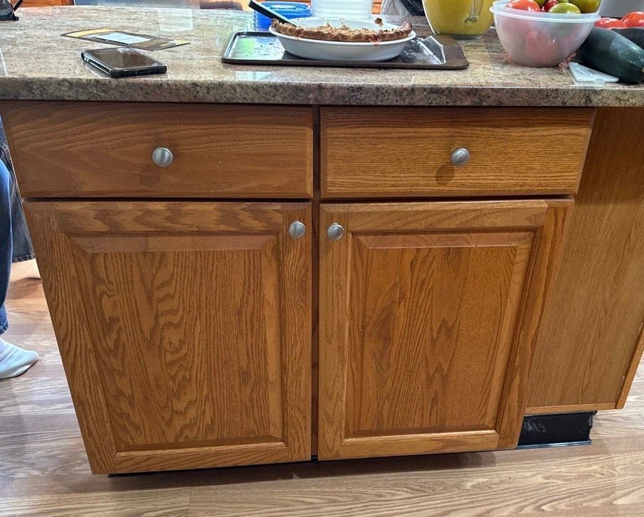 Wooden kitchen cabinet with drawers and doors, topped by a countertop with dishes and a fruit bowl.