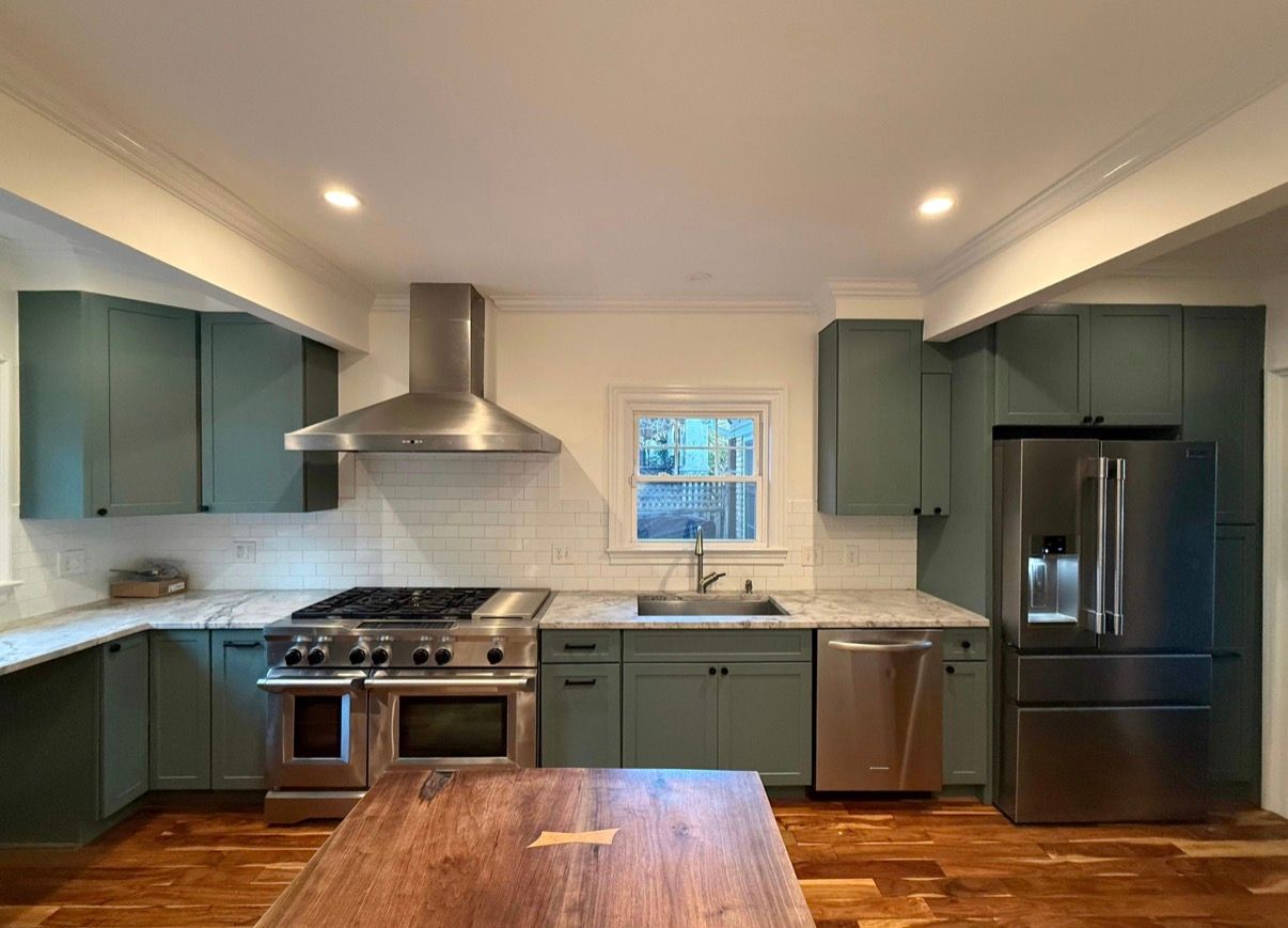 Modern kitchen with dark green cabinets, stainless steel appliances, white tile backsplash, and wooden island.