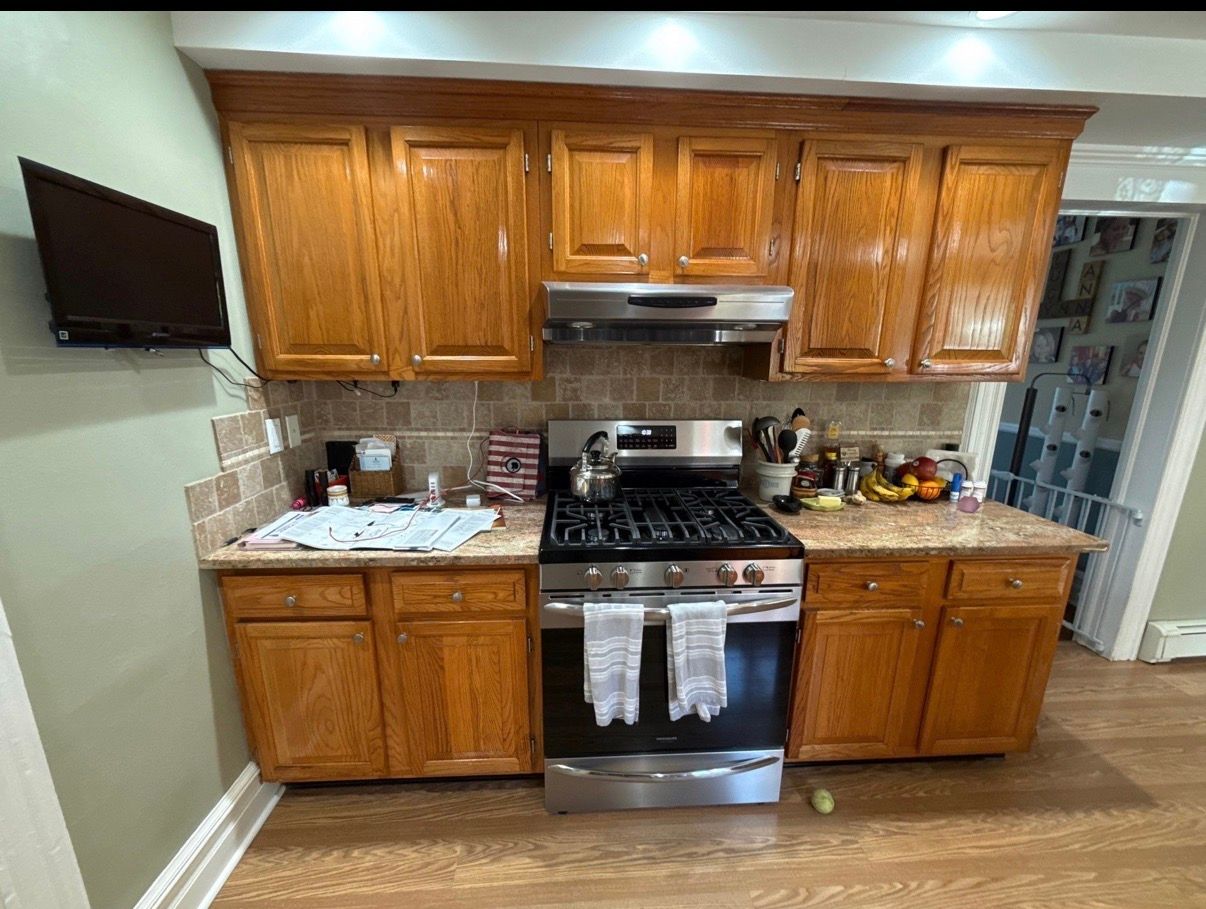 Kitchen with wooden cabinets, stainless steel stove, granite counters, and a wall-mounted TV on the left.