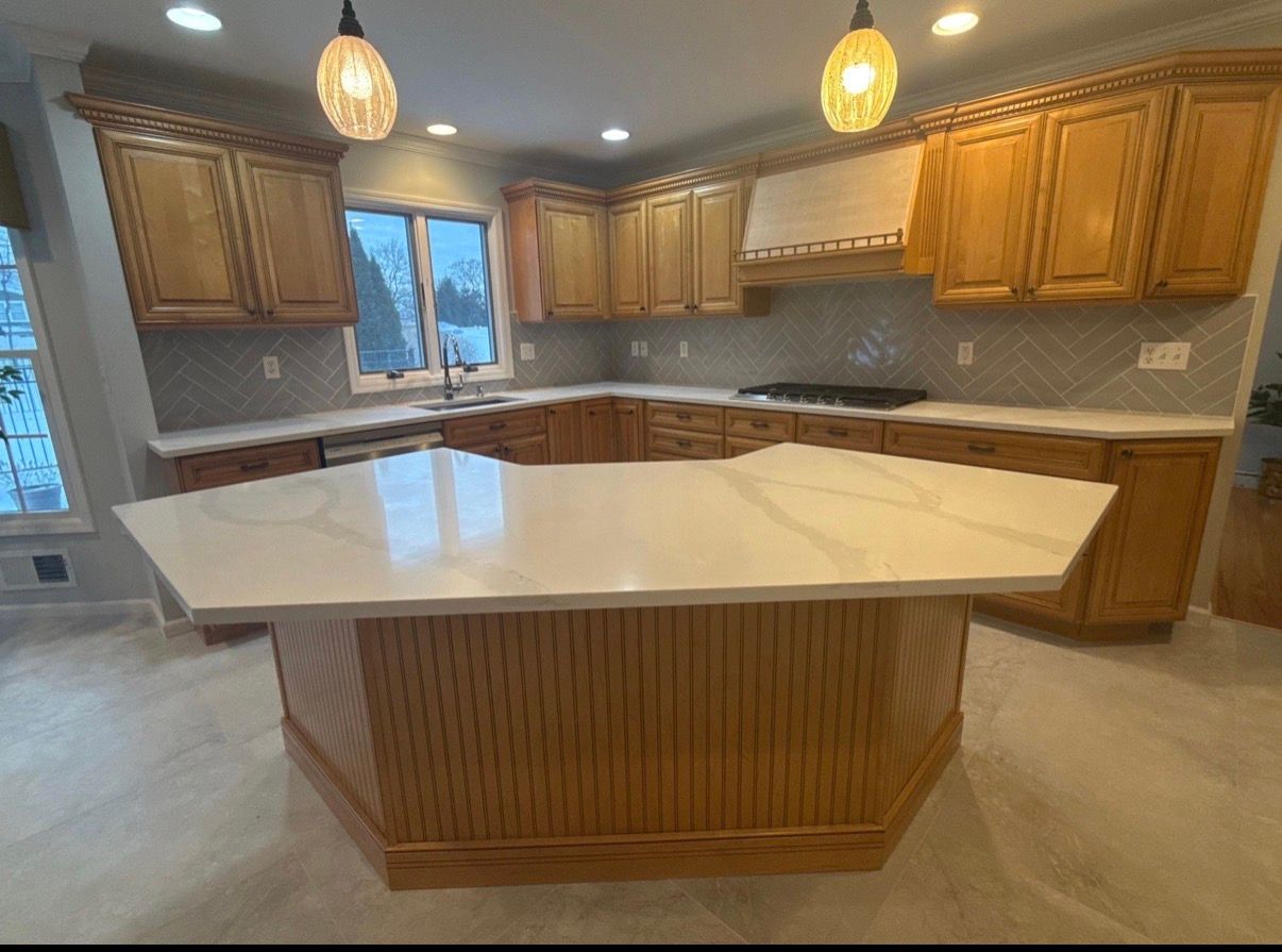 Spacious kitchen with wooden cabinets, white island countertop, and pendant lights.