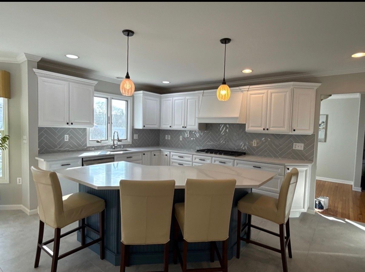 Bright kitchen with white cabinets, gray backsplash, island seating, and pendant lights
