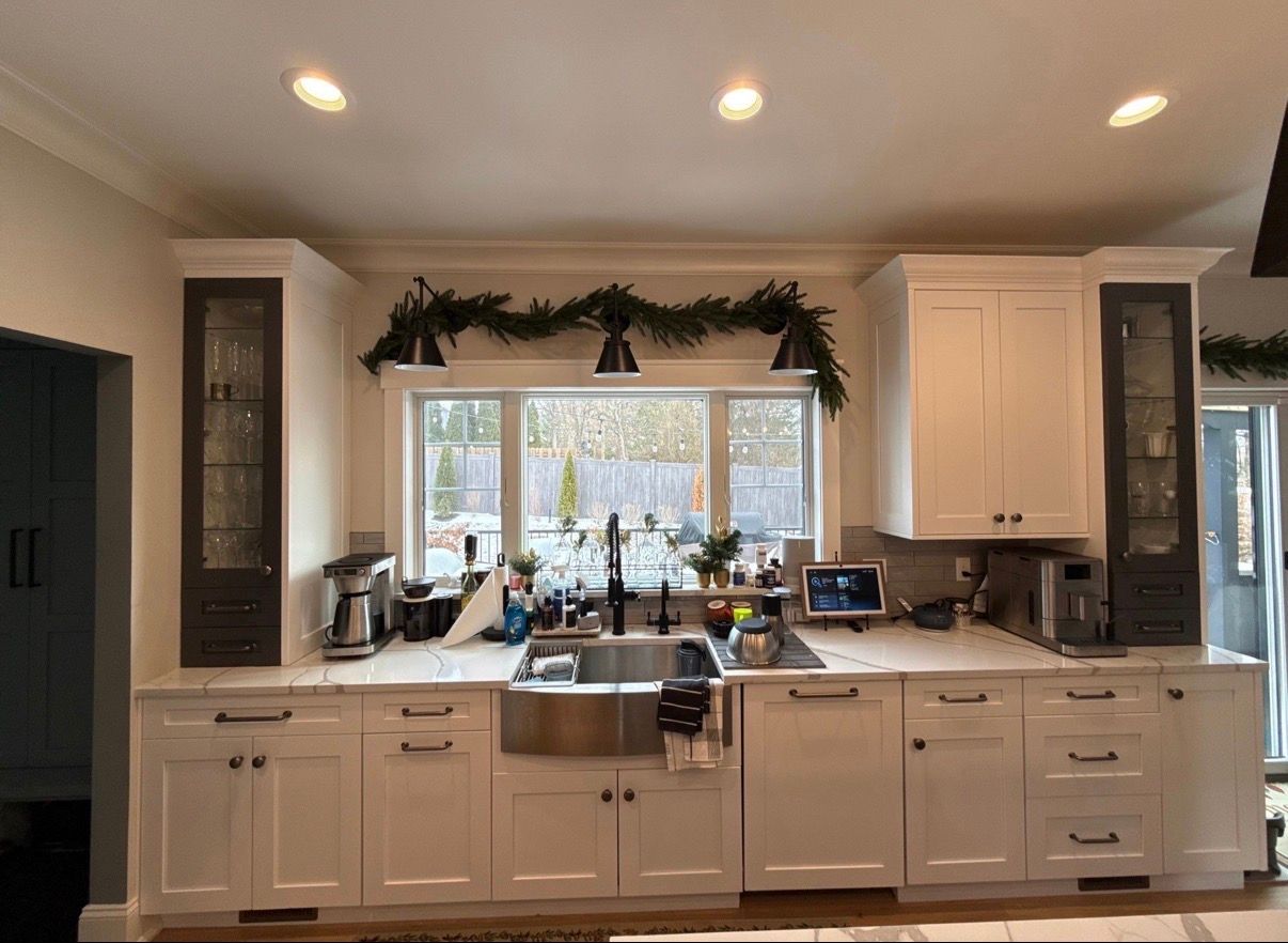 Bright white kitchen with a central sink, large window, recessed lights, and dark green garland above the window.