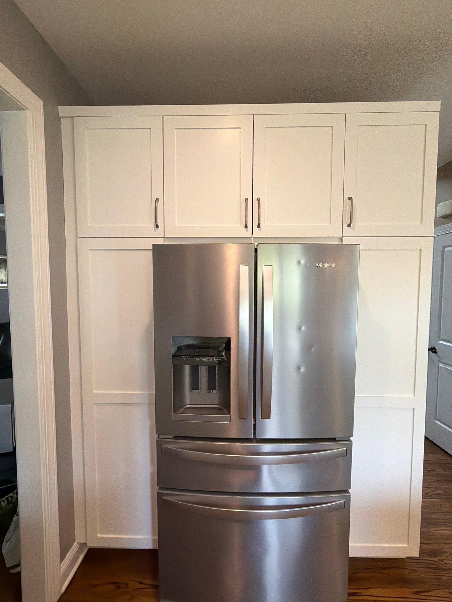 Stainless steel French-door refrigerator with water dispenser, framed by white kitchen cabinets.