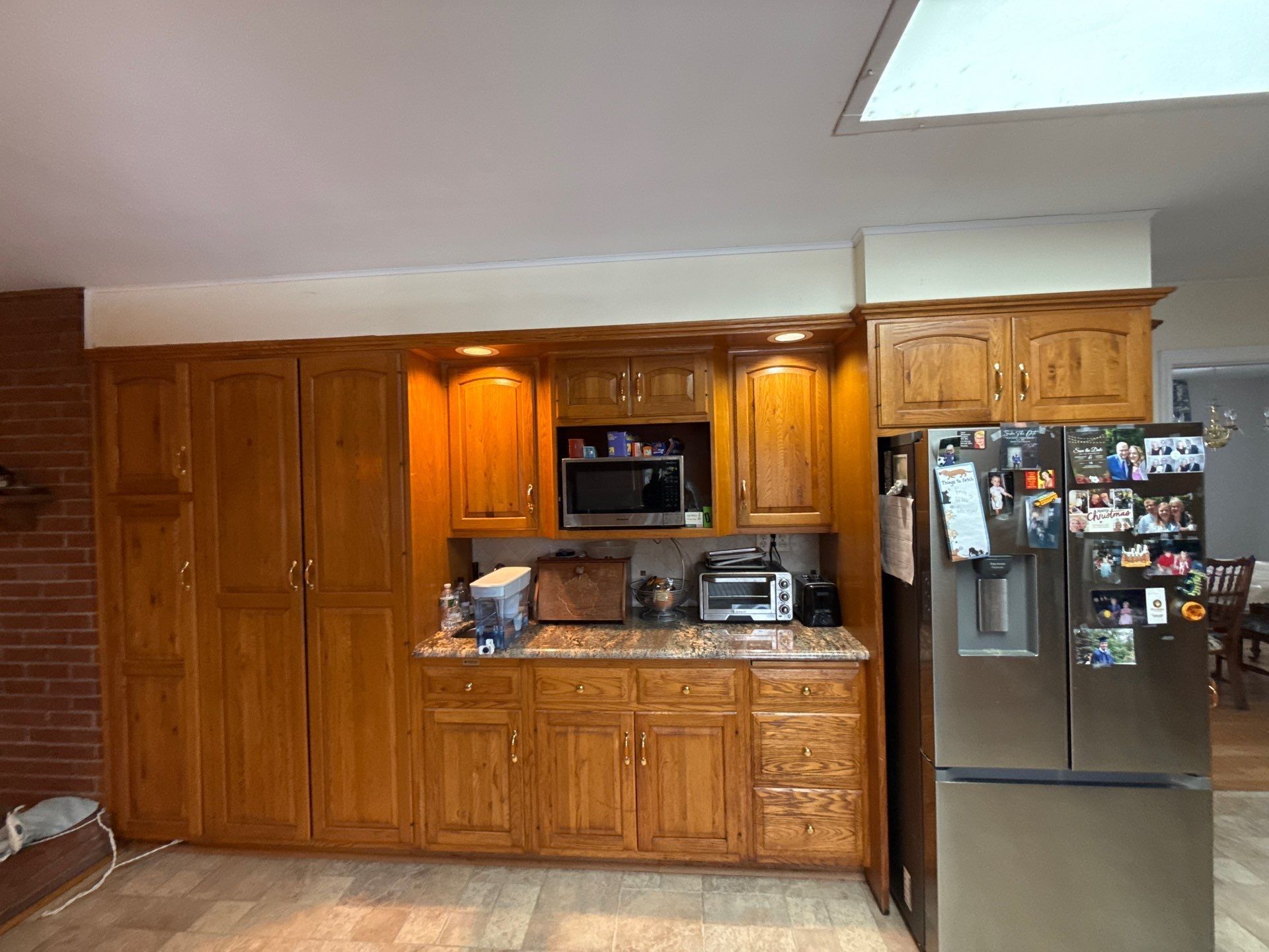White kitchen with cabinets, granite countertops, microwave, toaster oven, and stainless steel fridge