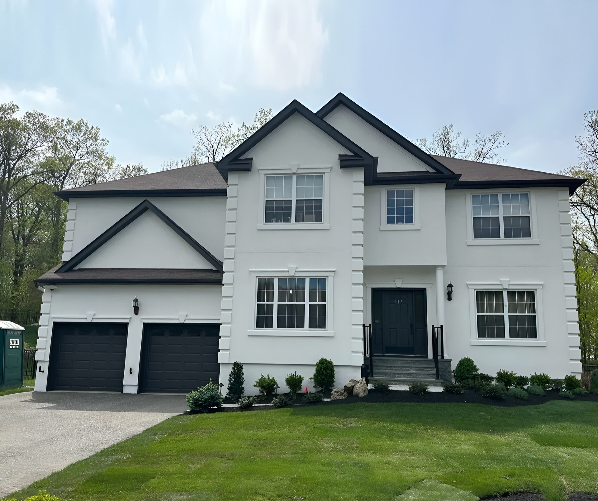 Two-story white suburban house with black trim, double garage, and green lawn under a blue sky.