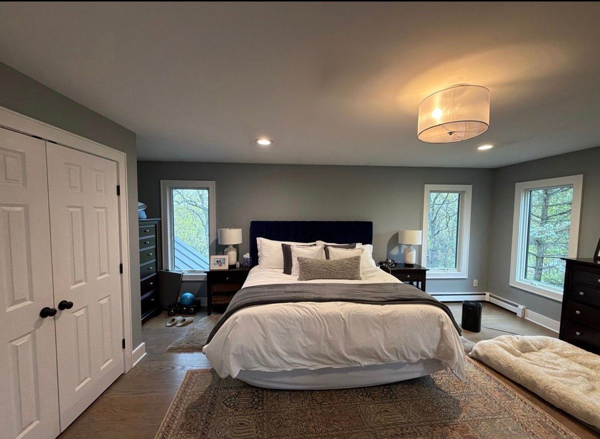 Neat bedroom with a large bed, gray walls, windows, nightstands, and a woven rug.