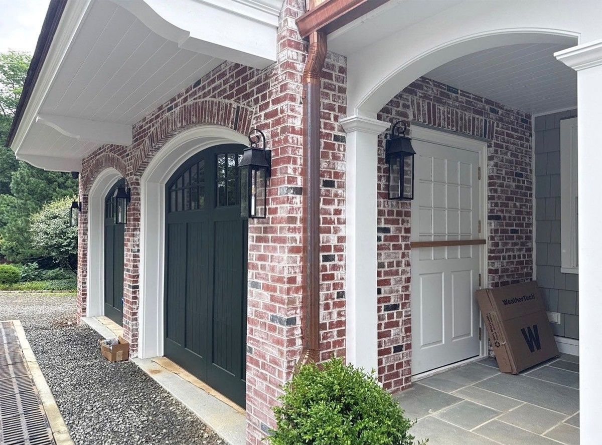 Brick house entryway with arched doors, white trim, and a red side door on a covered porch