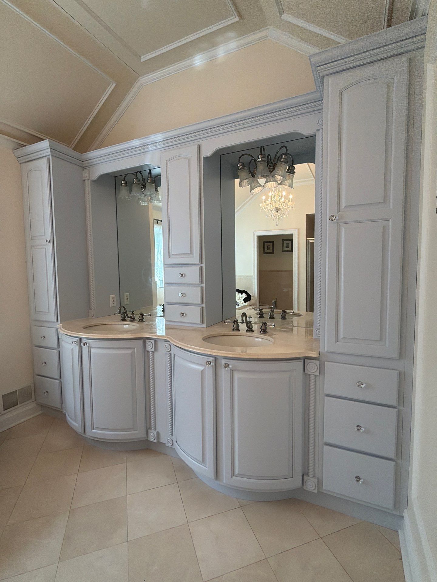 Elegant white bathroom vanity with double mirrors, marble countertop, and built-in cabinets under a sloped ceiling