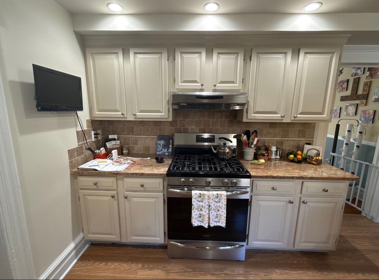 Bright kitchen with cream cabinets, stainless stove, granite counters, and a wall-mounted TV.