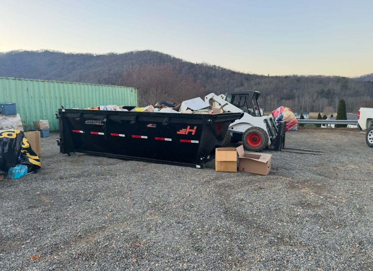 A dumpster is sitting in a gravel lot next to a forklift.