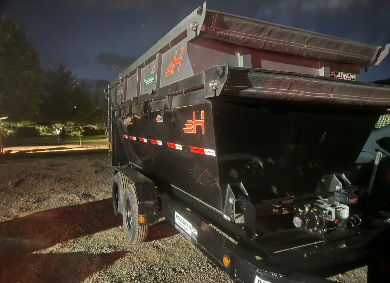 A dump truck is parked in a gravel lot at night.