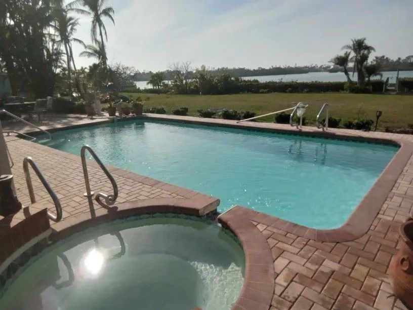 Swimming pool and jacuzzi with water view, palm trees, sunny day.