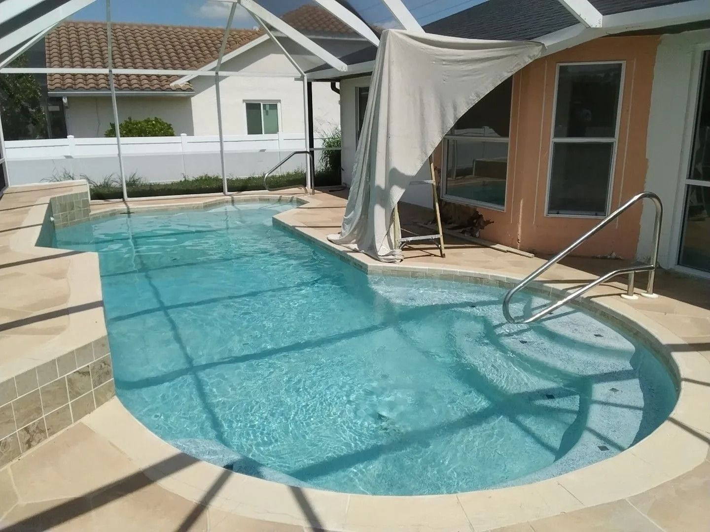 Swimming pool with light blue water and tan tiles, enclosed by a screen. A house is in the background.