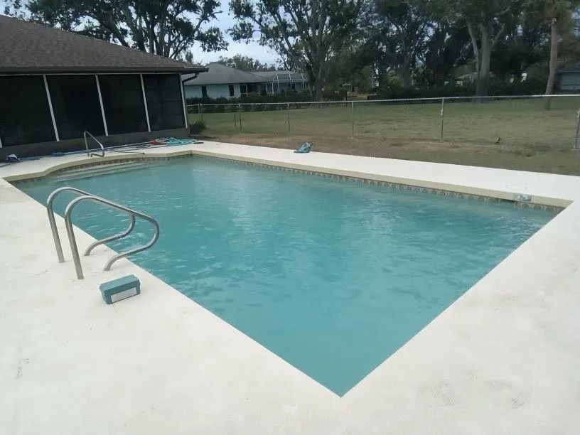Swimming pool with a light-colored deck, surrounded by a screened porch, grass, and a fence.