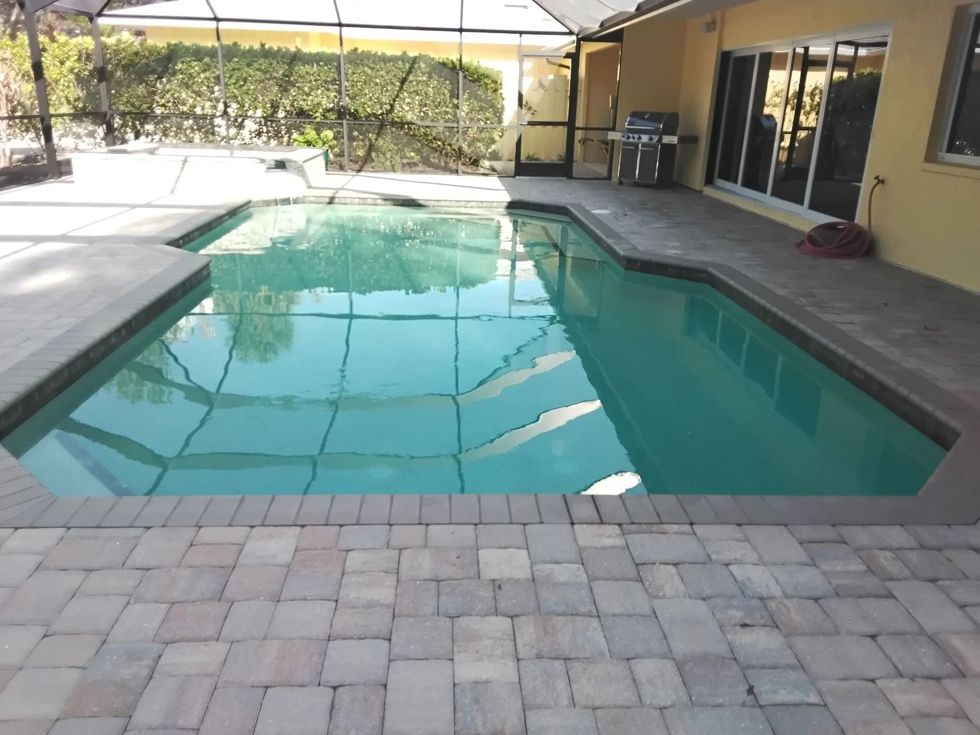 Swimming pool with blue water and surrounding patio. Yellow house in background.