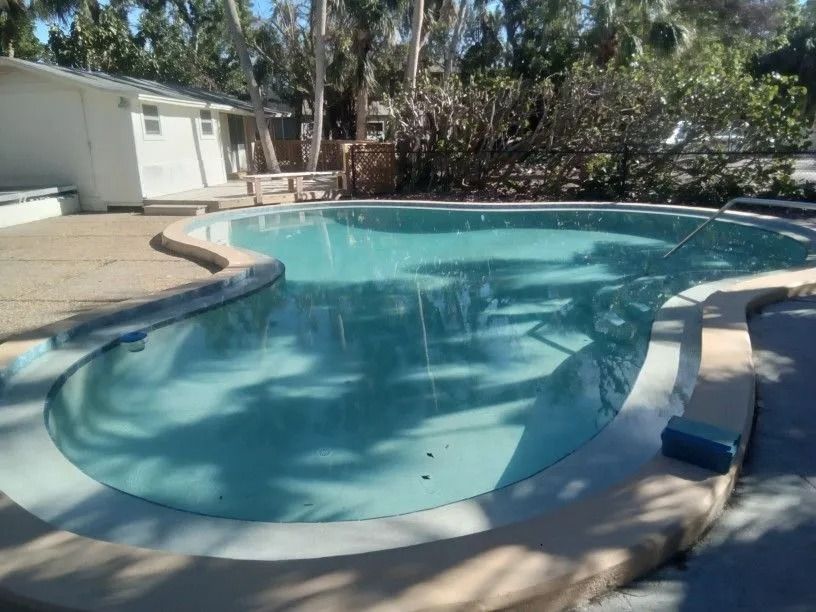 Swimming pool with a curved shape and light blue water, surrounded by concrete.