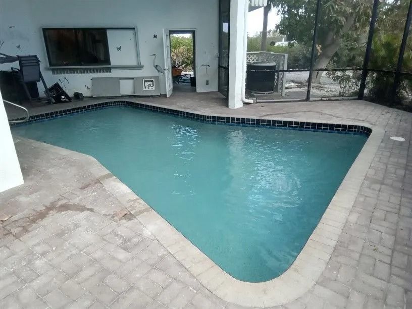 Pool with turquoise water surrounded by a brick patio, under a covered patio area.