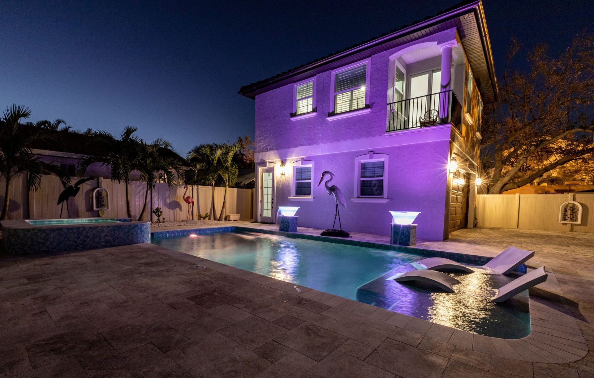 Night view of a house with a pool lit in turquoise, purple exterior lights.
