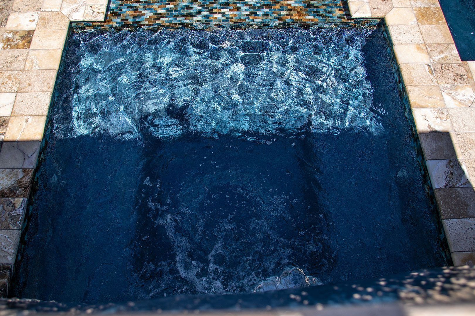 Pool with dark blue water cascading into a square basin; surrounding stone tiles.