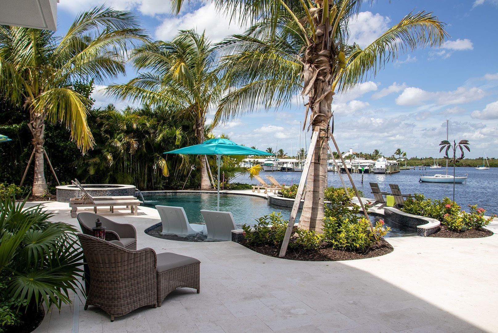 Poolside patio overlooking water with palm trees and lounge chairs.